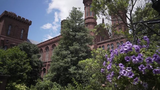 Steadicam shot walking through the gardens of the Smithsonian Institutions Castle Museum on a beautiful late spring day with blue sky and white clouds.