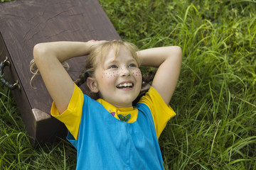 a fair-haired, freckled girl, lies on the grass, she has a suitcase under her head, she dreams of traveling.
