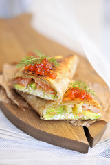 vegetarian dinner. rola with salmon and red caviar. with vegetables and avocado. with the addition of spices and green salad. On a wooden board in the form of fish.