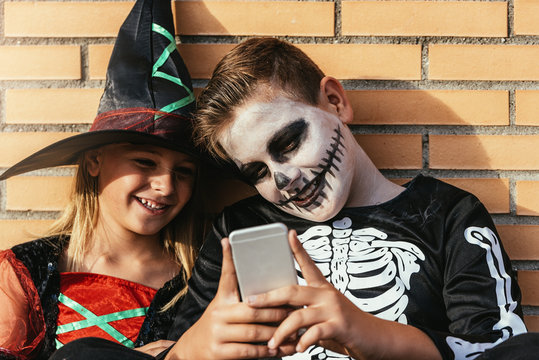 Happy Children Disguised Using The Mobile Phone In The Street.