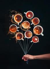 Bouquet of white coffee cups with splashes, looking like a bunch of balloons on a black background. Dynamic still life with barista hand. Greeting card.