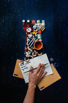 Fortress silhouette made from tiny objects, souvenirs and keepsakes. Writers hand and an open notebook with a quote Fortress round my heart. Conceptual still life with letters on a black background.