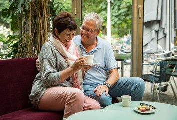 Senior couple in love sitting in cafe, drinking coffee, talking, laughing and having fun. Happy people in retirement concept.