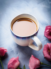 Fototapeta na wymiar Mug of coffee and pink flowers on blue background. Festive mother valentine day greeting card