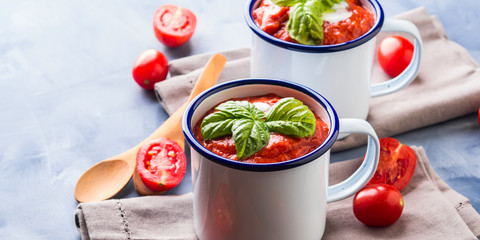 Creamy Tomato soup in enamel mugs on blue background