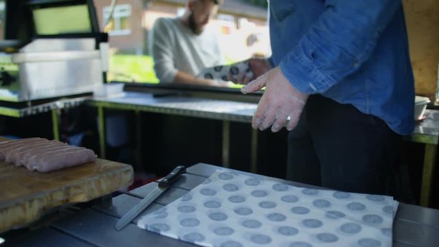  Street food vendor making hot dogs for customers at summer festival.