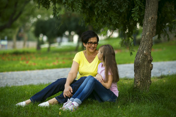 Grandmother sits with her granddaughter in a park on the grass looking at each other