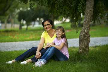 Fototapeta premium Grandmother sits with her granddaughter in a park on the grass