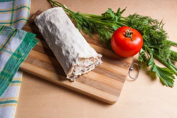 Pita bread or lavash wrapped with cottage cheese or curd, chicken, tomatoes and herbs - dill, onion, parsley on cutting board..