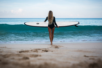 Beautiful young woman in bikini with surf board at beach of tropical island.