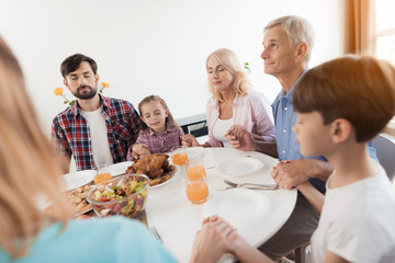 A man is sitting at a festive table for Thanksgiving and looking up. He is praying with his family