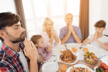 A man is sitting at a festive table and praying. Next to him sit his relatives and also pray