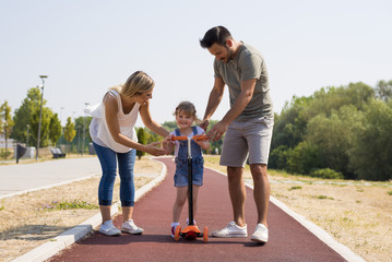 Young parents teaching daughter to ride a scooter for the first time