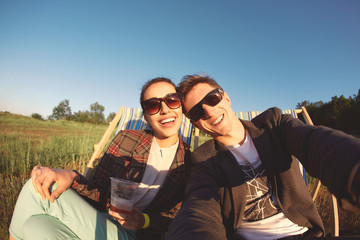 smiling couple in sun glasses makes selfie and sitting in a lounge chair at a picnic on a bright sunny day