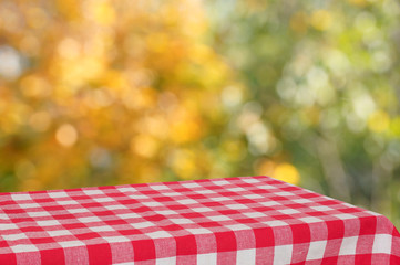 Empty table with a red checkered cloth in the autumn garden. Bright autumn colors. Blurred background. Free place for creativity. - 173936281