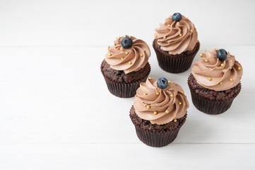Chocolate cupcakes with whipped chocolate cream, decorated fresh blueberry, gold confectionery sprinkling on white wooden table. Picture for a menu or a confectionery catalog. Top view.