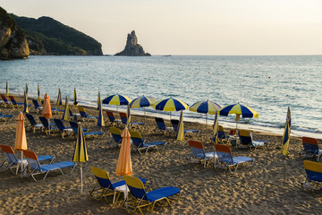 Umbrellas And Closed Parasols At Beach Next To Ionian Sea During Sunset