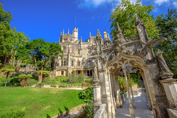 Gothic facade of grand house of Regaleira Palace, in Portuguese Quinta da Regaleira, and its gardens, famous landmark and Unesco Heritage in historic center of Sintra, Portugal. Sunny day, blue sky. © bennymarty