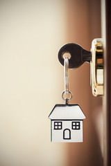 House key on a house shaped silver keyring in the lock of a door - 173942482