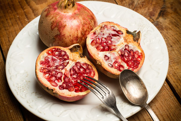 Granada fruta entera y corte por la mitad en plato redondo blanco con tenedor y cuchara de metal antigua. Vista superior