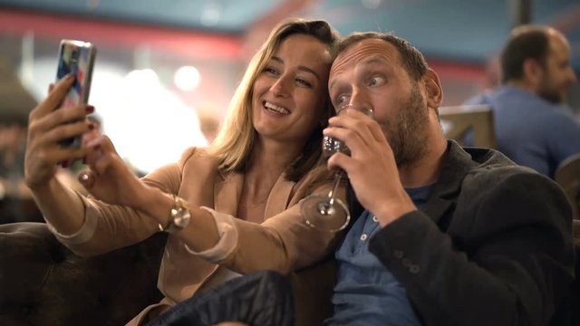 Young, happy couple taking selfie photos with cellphone sitting in cafe
