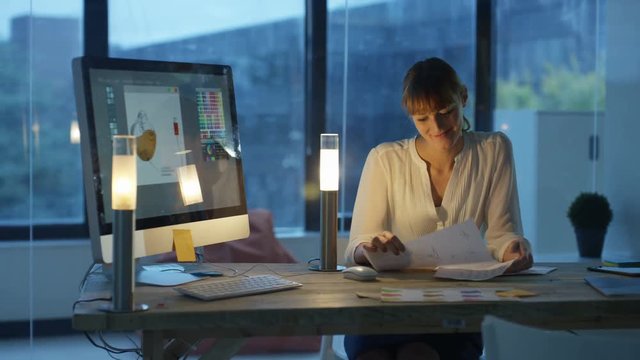 Designer working late in office, working on computer and making phone call