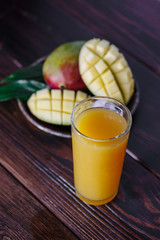 Fresh tropical mango juice on table with mango fruits on background.