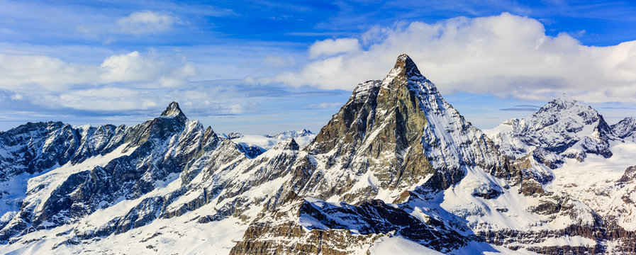 Panorama scenic view on snowy Matterhorn peak in sunny day with blue sky and clouds in background, Zermatt, Wallis, Switzerland.