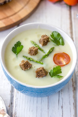 Beautiful asparagus cream soup with toasted bread on white wooden table.