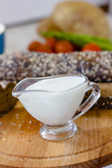 Cream sauce in a transparent glass bowl on wooden board.