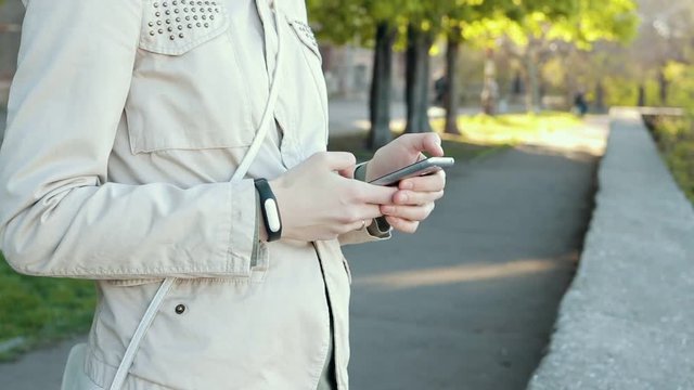 Girl in beige jacket using a mobile phone in the park