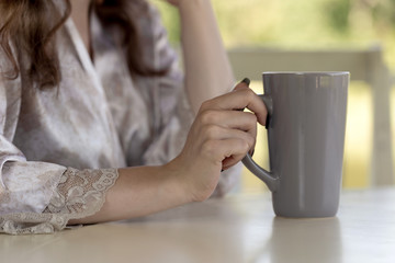 Woman's hands with long nails holding a big one-color gray cup. Pastel shades. Close shot.