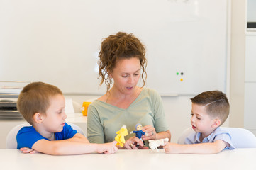 teacher woman playing with two child boy with finger puppets in the classroom