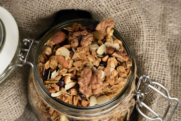Homemade granola in open glass jar on rustic wooden background