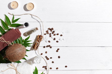 Natural spa set with candles, coffee beans, cinnamon, sea salt, oil, brown towel, coconut and green leaves on white wooden background