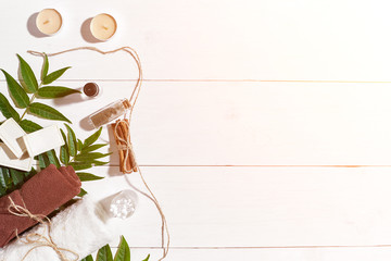 Natural handmade soaps with oil, cinnamon, candles, brown towel and green leaves on white wooden background. Sun flare