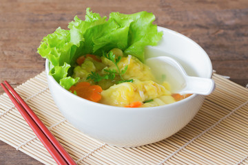 Homemade minced pork and shrimp wonton soup in white bowl on wood table for background. Delicious wonton in clear soup for breakfast or lunch or dinner. Wonton or dumpling is popular Chinese food.