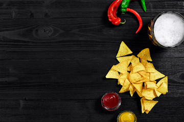 Snack for party, chips, nachos with sauces: tomato ketchup , mustard and mug of beer on a black background. Top view, copy space
