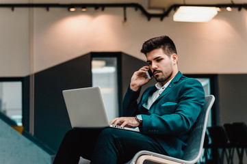 Handsome businessman speaking on the phone and working with laptop in office.