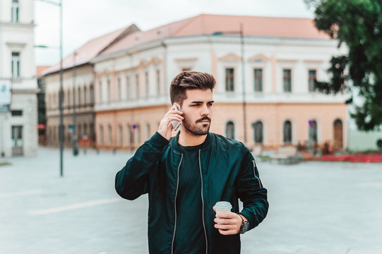 Handsome Businessman Talking On Phone While Holding A Cup Of Coffee Outside.