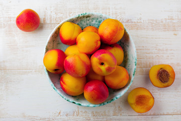Naklejka na ściany i meble Fresh juicy fruit nectarines in ceramic bowl on white wooden background. Selective focus. Top view. Rustic style.
