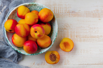 Fresh juicy fruit nectarines in ceramic bowl  on  white wooden background. Selective focus. Top view. Rustic style.