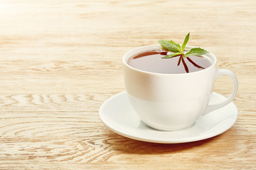 Cup of mint tea and green leaves on light table