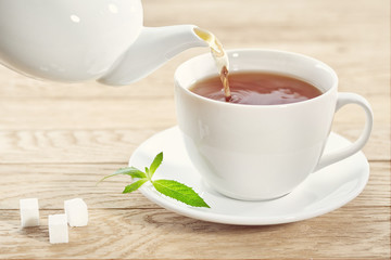 cup with green tea, sugar and teapot on light wooden table background