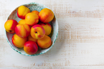 Fresh juicy fruit nectarines in ceramic bowl  on  white wooden background. Selective focus. Top view. Rustic style.