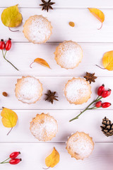 Flat lay in autumn style. Delicious cupcakes with cinnamon sticks, anise stars, berries of rosehip and autumn leaves on white wooden background.