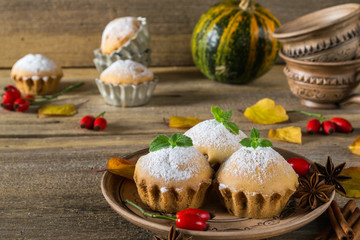 Autumn pastries. Homemade cupcakes with powdered sugar on a plate with cinnamon sticks, anise stars, pumpkins, berries of rose hip and autumn leaves 