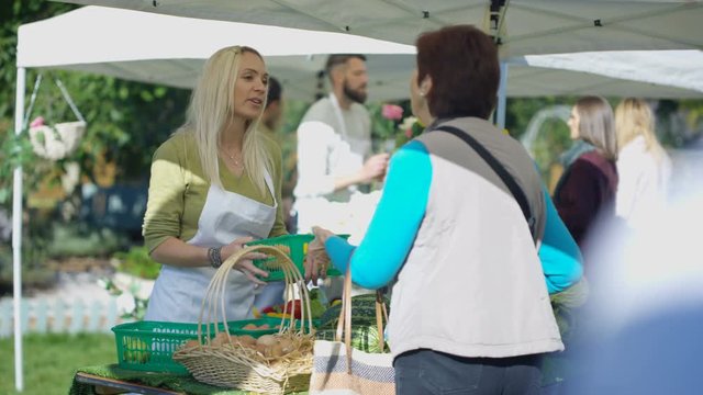  Cheerful woman selling fresh fruit & veg to customers at farmers market