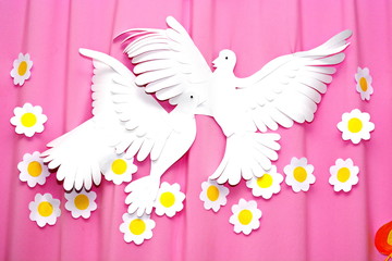 fluttering white paper peace doves on a pink woven background with flowers