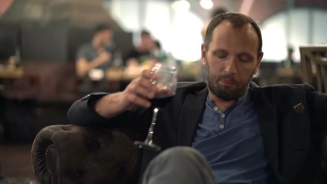 Drunk man drinking red wine sitting on sofa in cafe 
